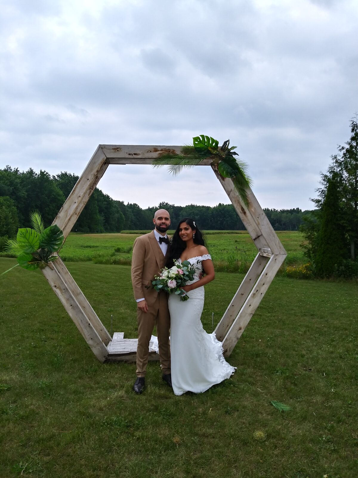 A newly married couple standing beneath a wooden ceremony arch