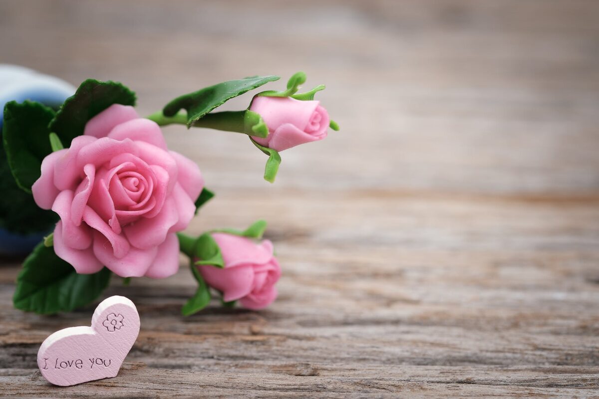 Pink roses beside a small wooden heart engraved with love you